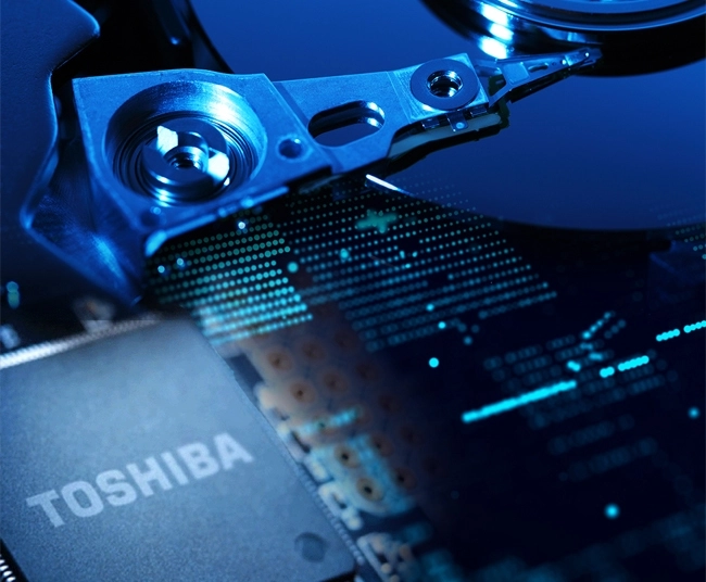 Close-up of a Toshiba semiconductor chip overlaid on the internal components of a hard drive, illustrating Toshiba’s advanced semiconductors and data storage solutions.